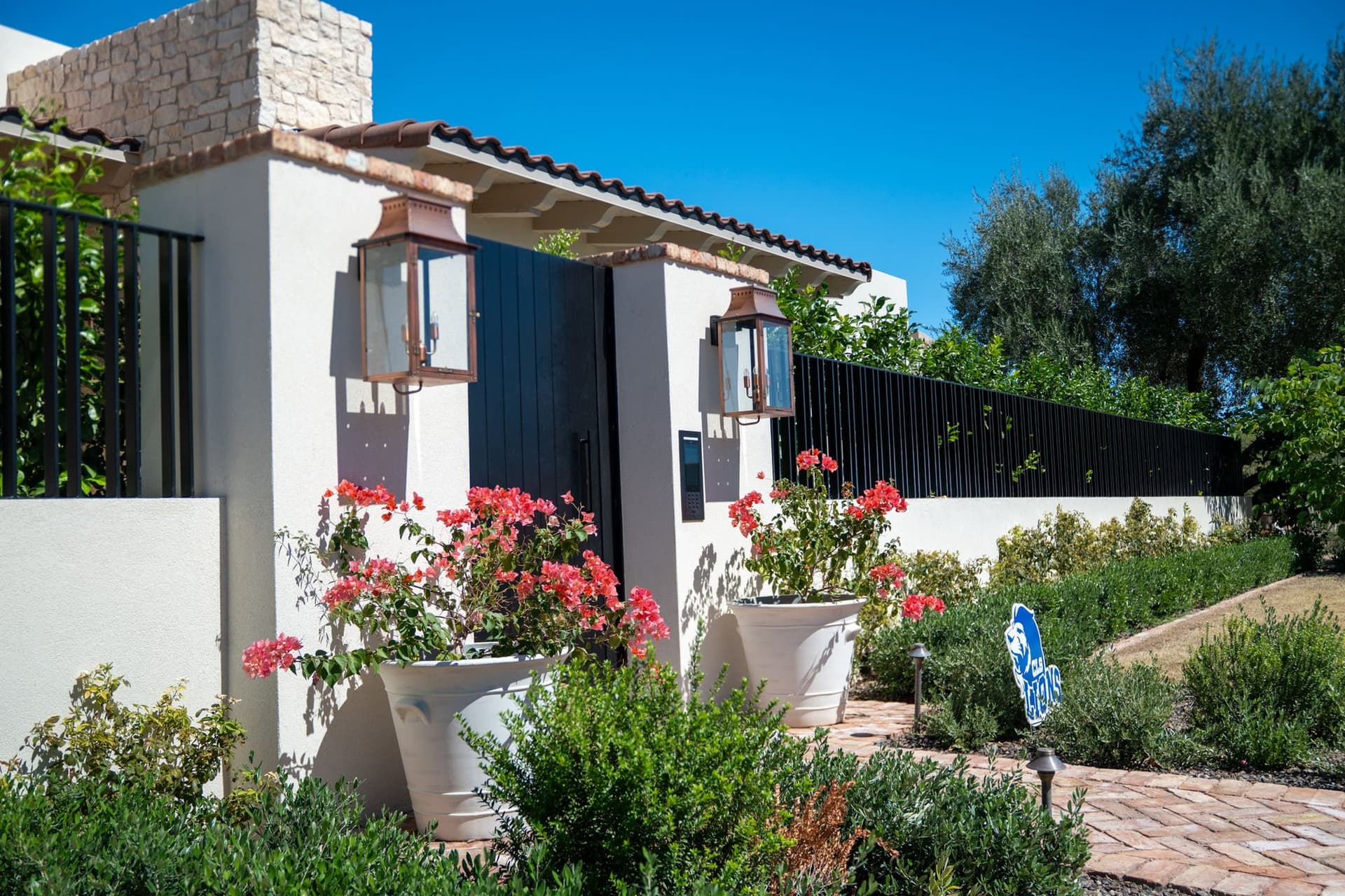 White stucco entrance columns with copper lanterns and flowering landscaping