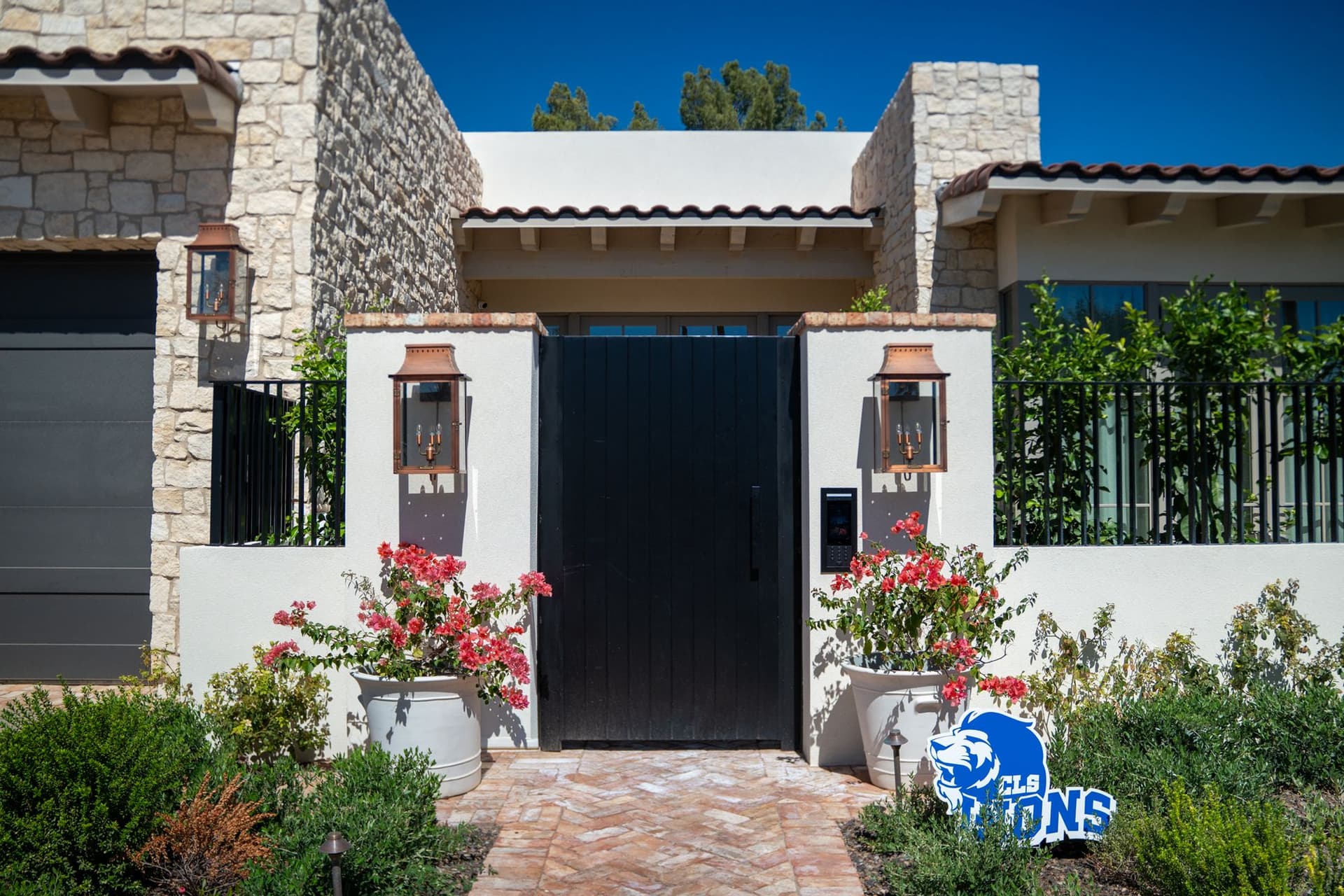 Black courtyard gate framed by white stucco columns and stone exterior walls