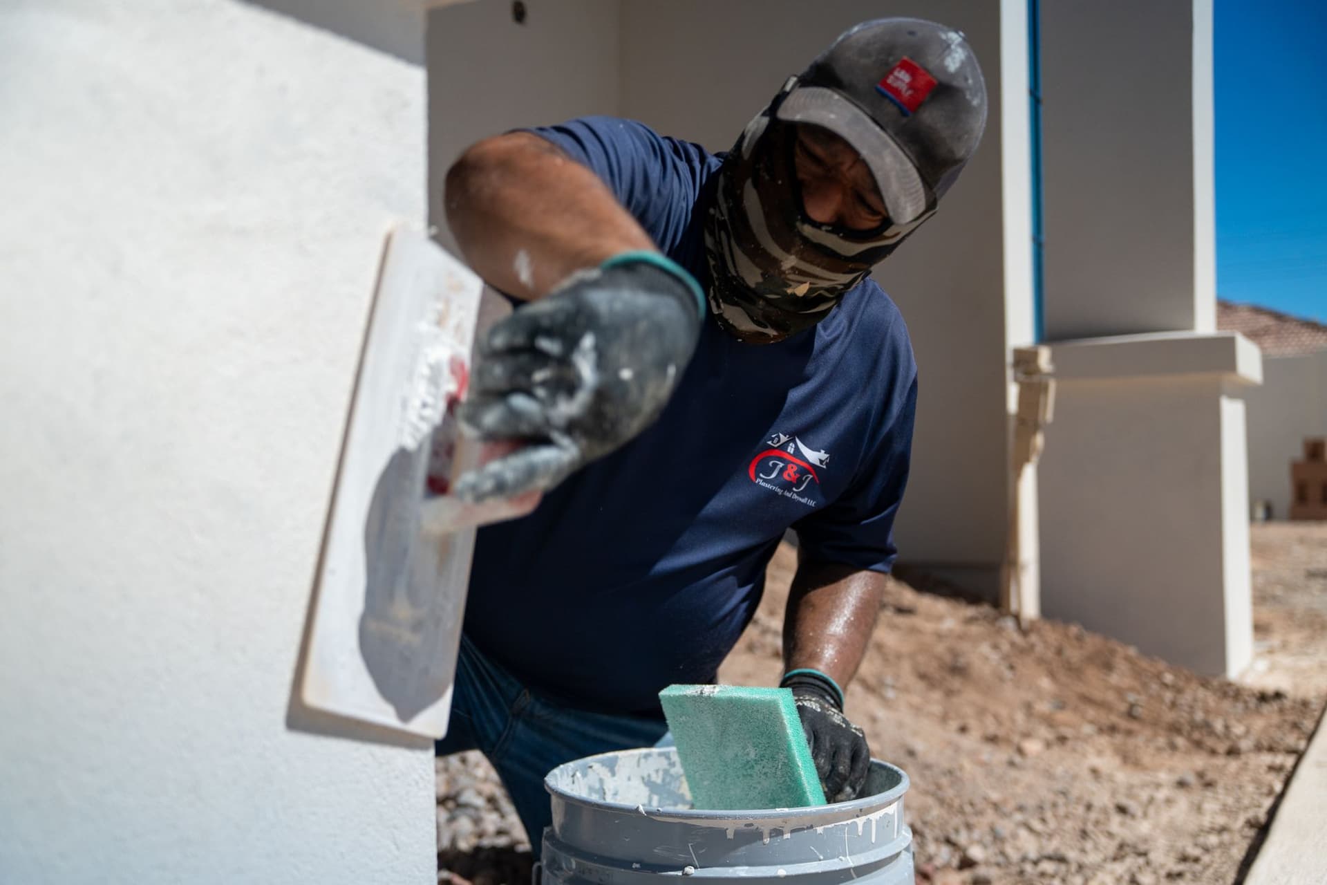J&J Pros crew member in a branded shirt troweling an exterior stucco column